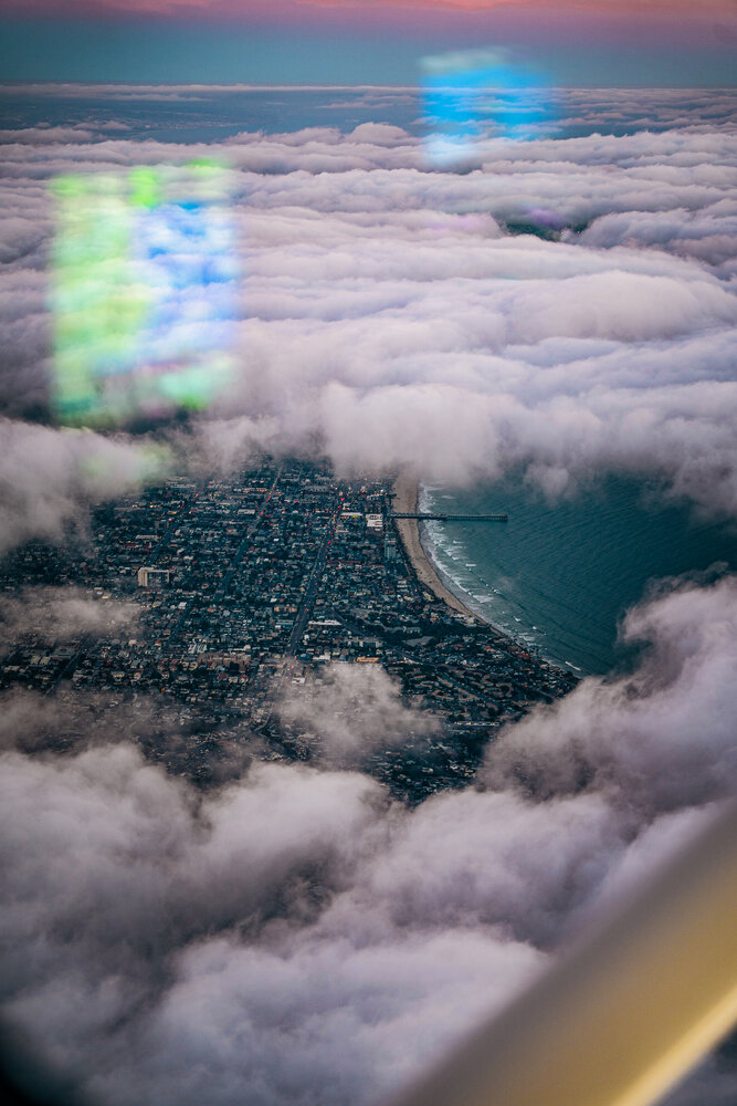 Coastal city and pier seen through breaking clouds from the air